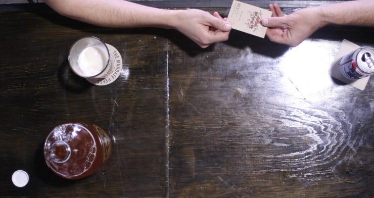 two people hand a letterpress business card over a table while drinking