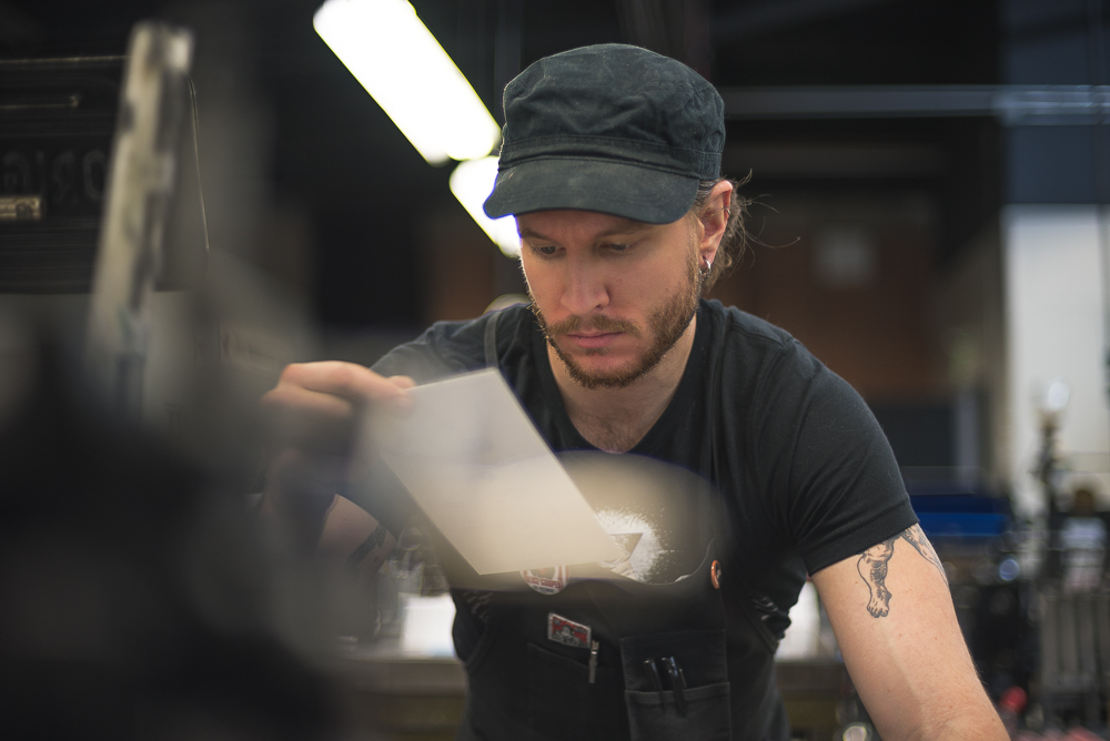 Gabriel Danilchik checking quality of letterpress print while operating press