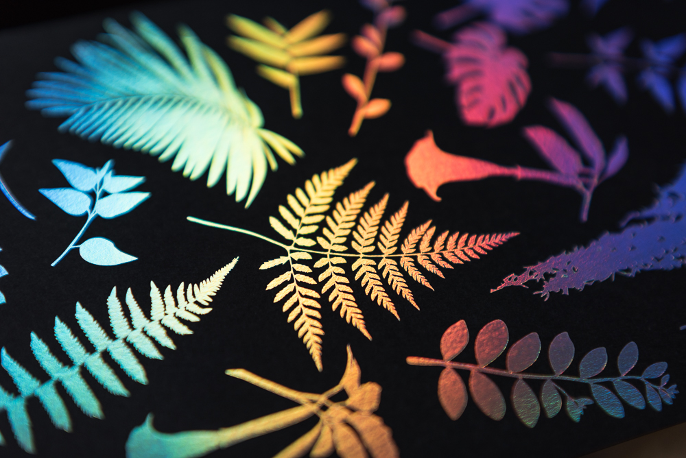 letterpress printed leaves on black paper with holographic foil shown at angle with color