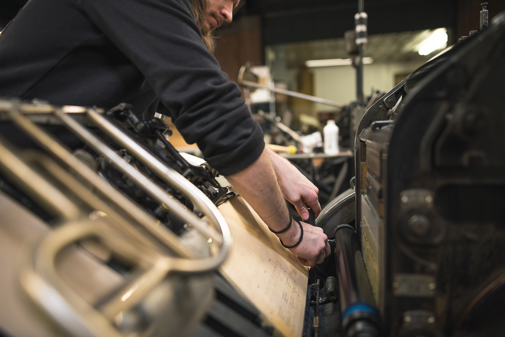 man adjusts guides of letterpress printing press at The Mandate Press 